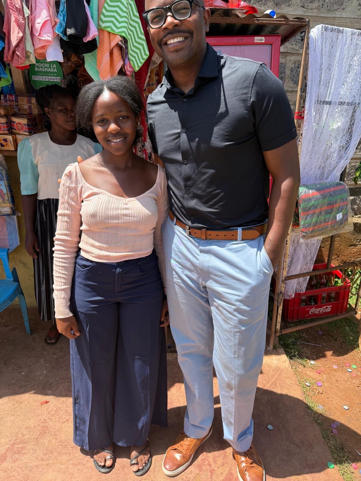 A Soma Initiative student smiling alongside a programme lead outside her family's shop