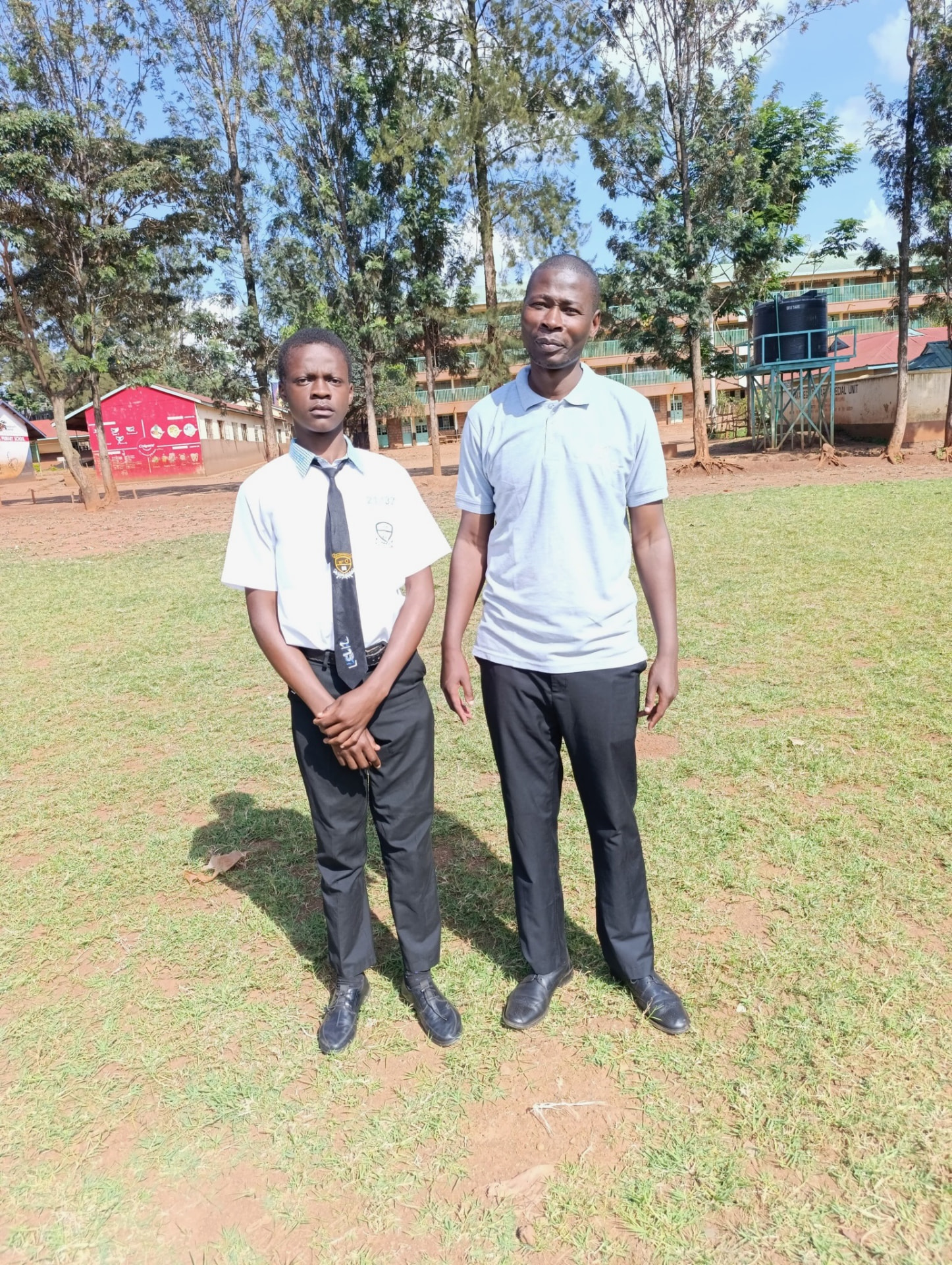 A secondary school student in uniform standing with his Soma Initiative coordinator